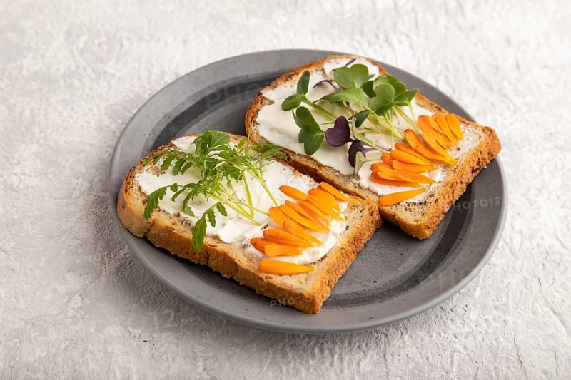 White bread sandwiches with cream cheese, calendula petals and microgreen radish and tagetes on gray concrete background. side view, close up