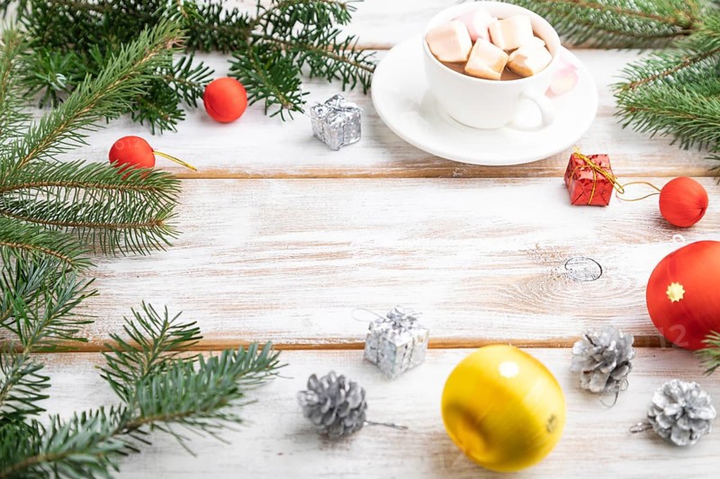 Christmas or New Year frame composition. Decorations, red balls, cones, fir and spruce branches, cup of coffee, on a white wooden background. Side view, copy space