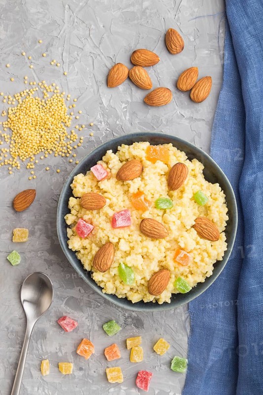 Millet porridge with candied fruits and almonds in blue ceramic bowl on a gray concrete background and blue linen textile. Top view, flat lay, close up