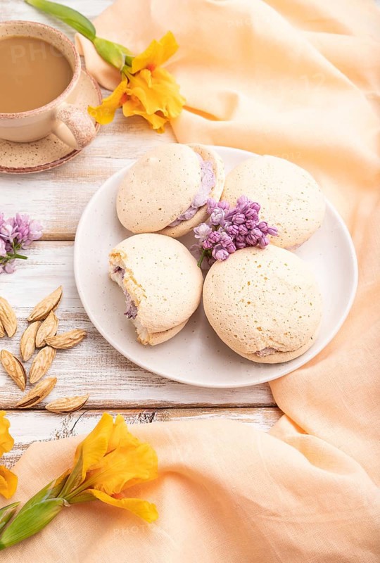 Meringues cakes with cup of coffee on a white wooden background and orange linen textile. Side view, close up