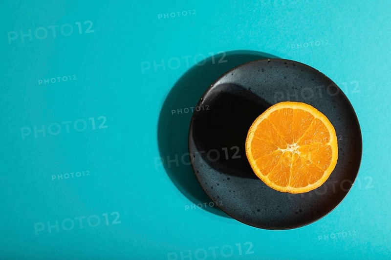 Ripe cut orange on blue ceramic plate on blue pastel background. Top view, flat lay, copy space, hard light. Tropical, healthy food, concept, minimalism