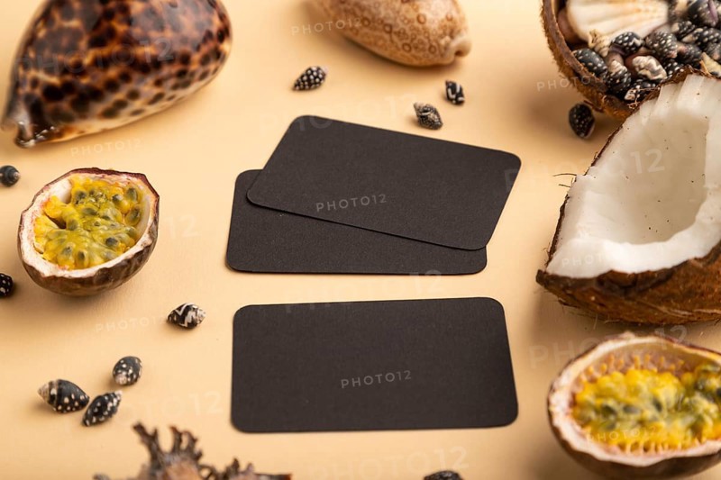Brown paper business card with coconut, passion fruit, seashells, on orange pastel background. Side view, copy space. Tropical, healthy food, vacation, holidays concept