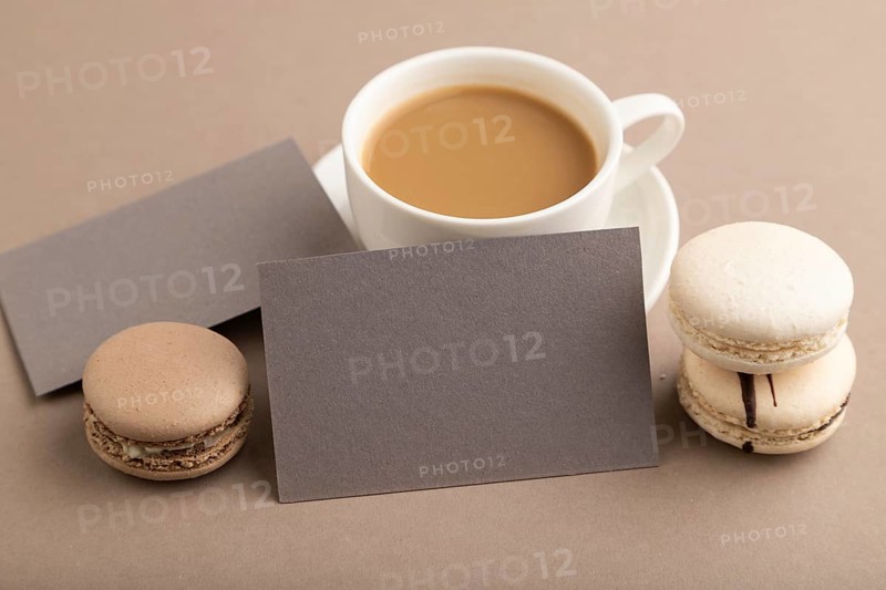 Gray paper business card mockup with brown and white macaroons and cup of coffee on beige pastel background. Blank, side view, copy space, still life, close up. morning, breakfast concept