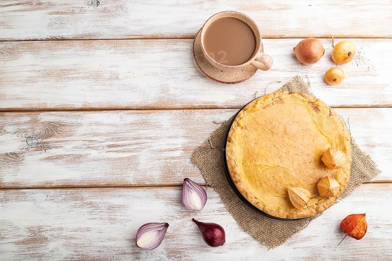 Autumn onion pie and cup of coffee on white wooden background and linen textile. Top view, flat lay, copy space