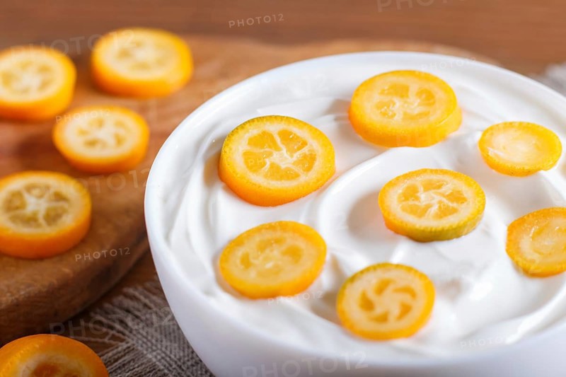 Greek yogurt with kumquat pieces in a white plate on a brown wooden background, close up
