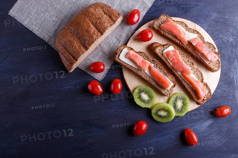 Smoked salmon sandwiches with butter on dark wooden background. cherry tomatoes. top view, copy space