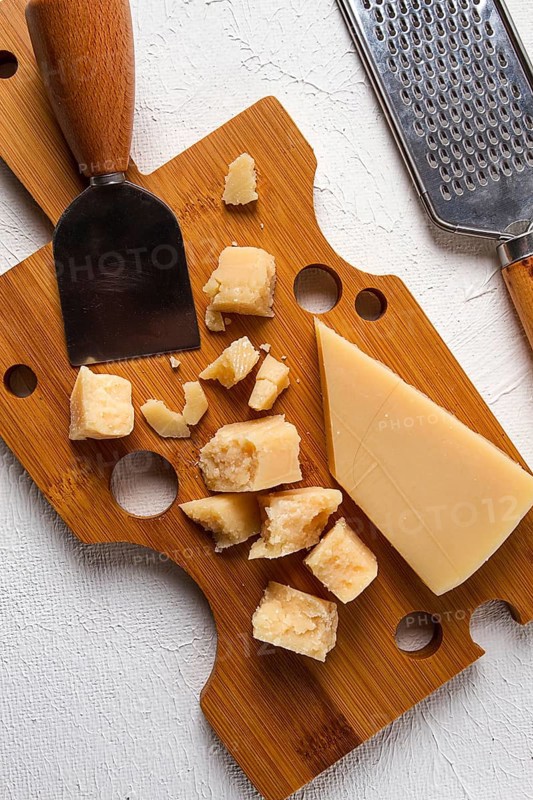Hard cheese, parmesan, on a cutting board, cheese knife, grater, top view, no people
