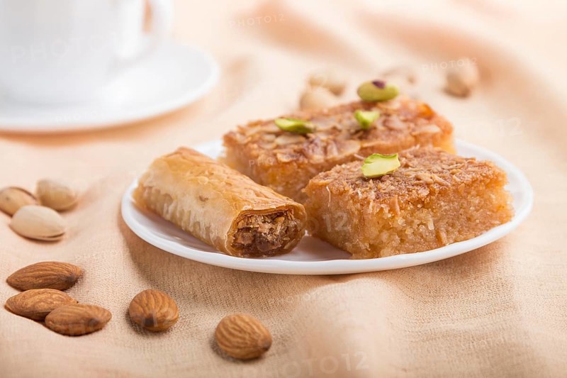 Traditional arabic sweets (basbus, kunafa, baklava) and a cup of coffee on a gray concrete background and orange textile. side view, close up, selective focus, macro