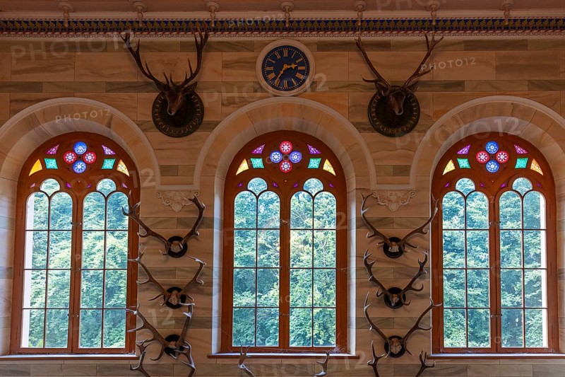 Stained glass window with antlers as wall decoration and a classical clock, Rügen, Granitz Castle