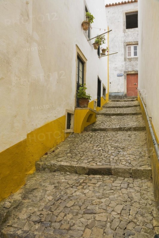 Old street with mosaic style paving stone stairs and white roughcast buildings with yellow painted stripes, Medieval city of Obidos, Portugal, Europe