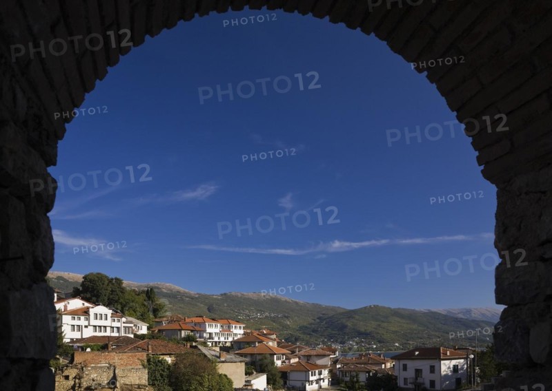Residential buildings with terracotta ceramic tiled rooftops and mountain range viewed through a brick arch, Town of Ohrid, Macedonia, Europe