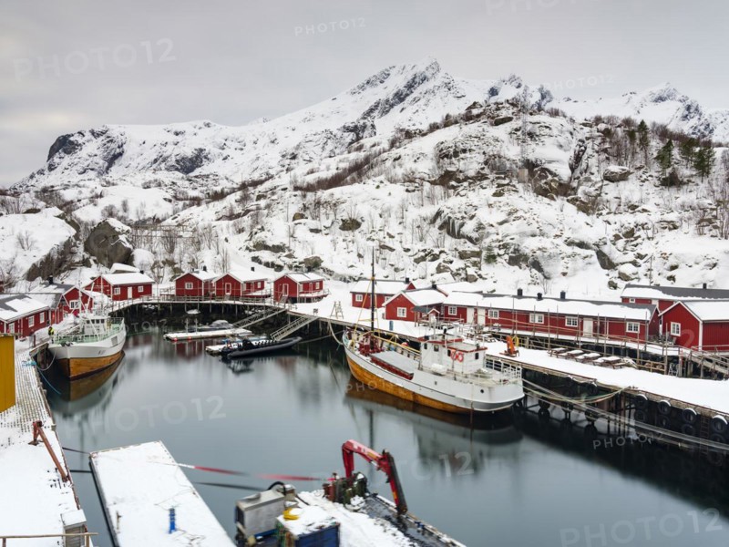 Red wooden houses in the harbour of the authentic fishing village of Nusfjord, snow-capped mountains in the background, Flakstadøya, Lofoten, Norway, Europe