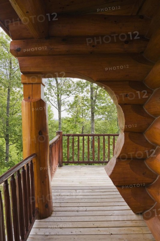 Brown reddish stained Scandinavian log cabin home with arch and wall made of large chinked logs and wood plank veranda in summer, Quebec, Canada, North America