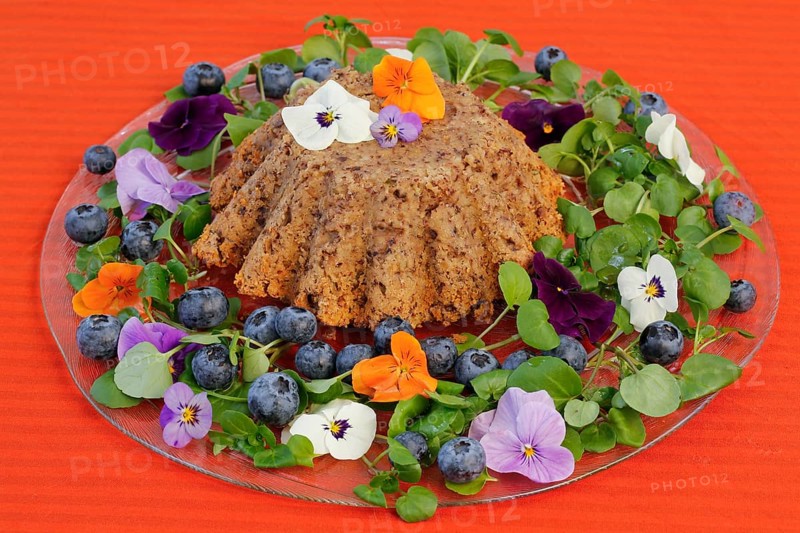 Vegetarian cuisine, chestnut roast, chestnut cake, chestnut roast, chestnut cake with hazelnuts, chestnut cake, savoury, vegan, salty, baked, from the oven, healthy, main course, glass plate, new cuisine, decoration with pansies, violet (Viola), blueberries (Vaccinium), blueberries, food photography, studio, Germany, Europe
