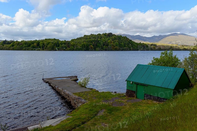A scenic lake view with a green shed beside a dock, surrounded by hills, trees, and a partly cloudy sky, Loch Awe, Scotland, United Kingdom, Europe