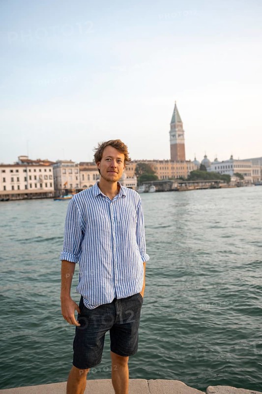 Young man in striped shirt and shorts on the banks of the Grand Canal, behind Campanile, Venice, Veneto, Italy, Europe