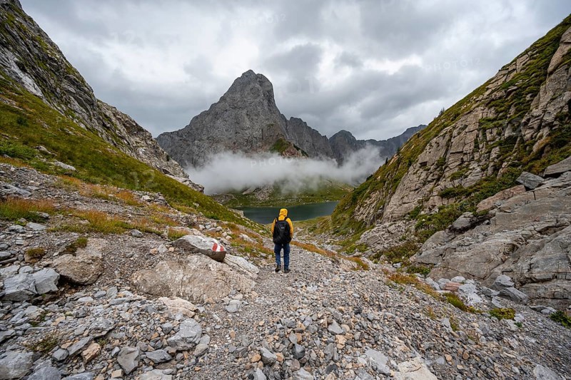 Mountaineers on a hiking trail with a view of rocky cloudy mountains and Wolayersee, hiking trail to Wolayerseehütte, cloudy mountain peaks, Carnic Alps, Carnic High Trail, Carinthia, Austria, Europe