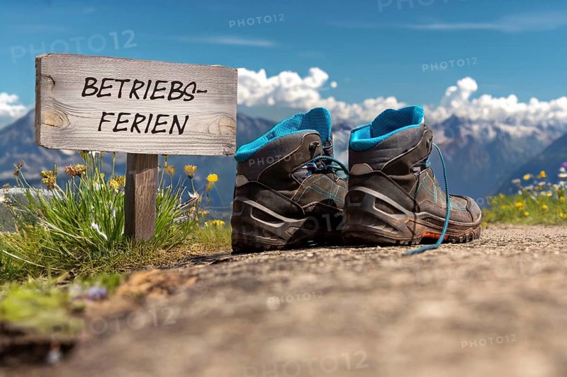 Symbolic image of company holidays/summer holidays: Hiking boots in front of an alpine backdrop and a sign with the inscription BETRIEBSFERIEN (company holidays)