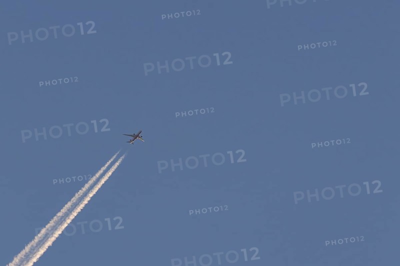 Boeing 787-8 Dreamliner aircraft flying across a blue sky with a vapour trail or contrail behind, England, United Kingdom, Europe
