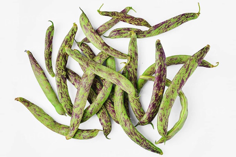 A vibrant collection of freshly harvested purple green beans sprawled across a surface, showcasing their unique colors and textures. Perfect for cooking, salads, or preserving for later use