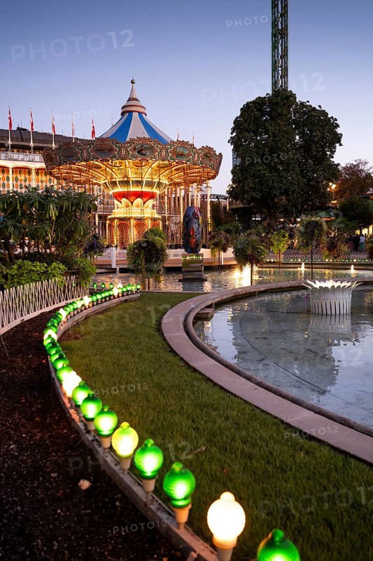Illuminated historical carousel, garden with pond and lights, dusk, Tivoli Amusement and Recreation Park, Copenhagen, Denmark, Europe