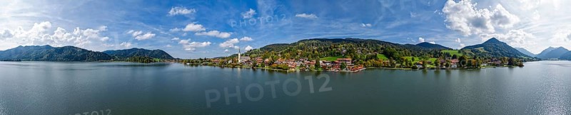 Painter's panoramic view of a Bavarian village on a lake, surrounded by mountains under a blue sky with clouds, Schliersee