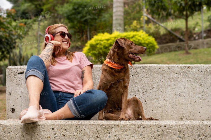 Portrait of a beautiful young woman enjoying outdoors and listening to music, accompanied by her pet