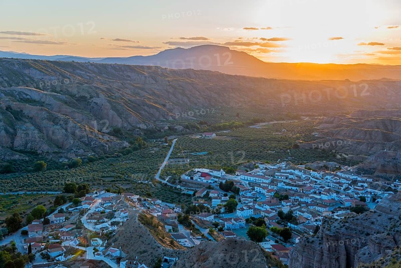 A village lies in a valley surrounded by hills and mountains as the sun sets and the valley glows in warm light, Gorafe, Guadix, Granada, Andalusia, Spain, Europe