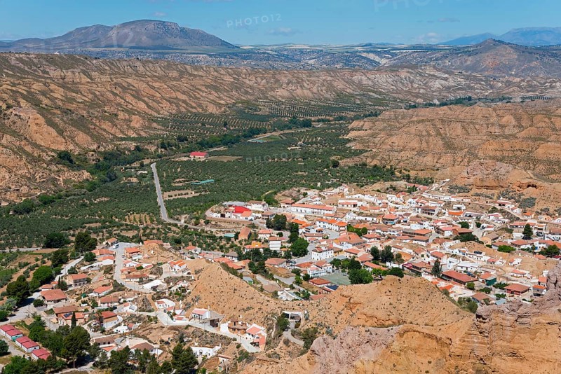 A small village with orange-coloured roofs is nestled in a green valley surrounded by mountains under a blue sky, Gorafe, Guadix, Granada, Andalusia, Spain, Europe