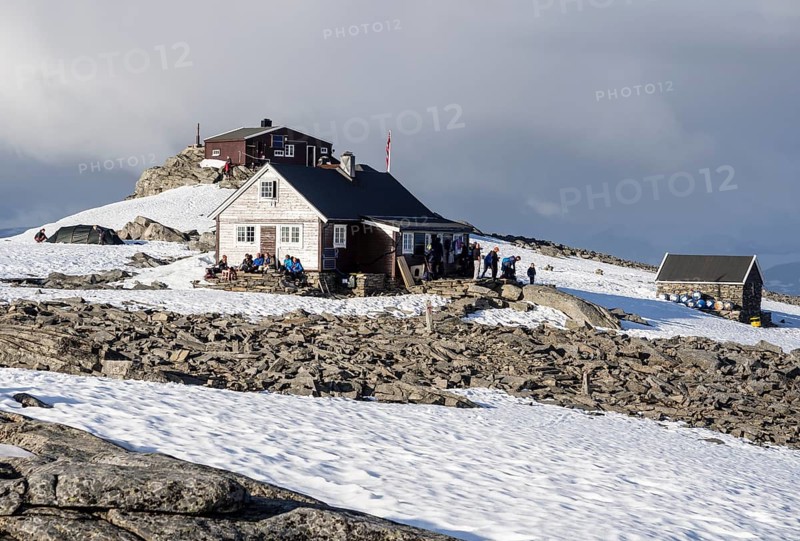 Mountain hut on top of mountain Fannaråken, hikers sit outside the hut, enjoy the sun, Jotunheimen National Park, Norway, Europe
