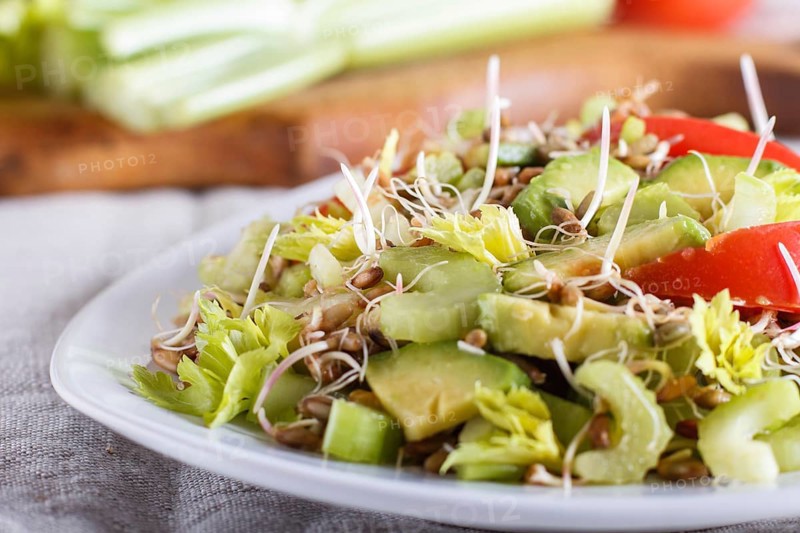 Vegetarian salad of celery, germinated rye, tomatoes and avocado on linen tablecloth, close up, selective focus, side view