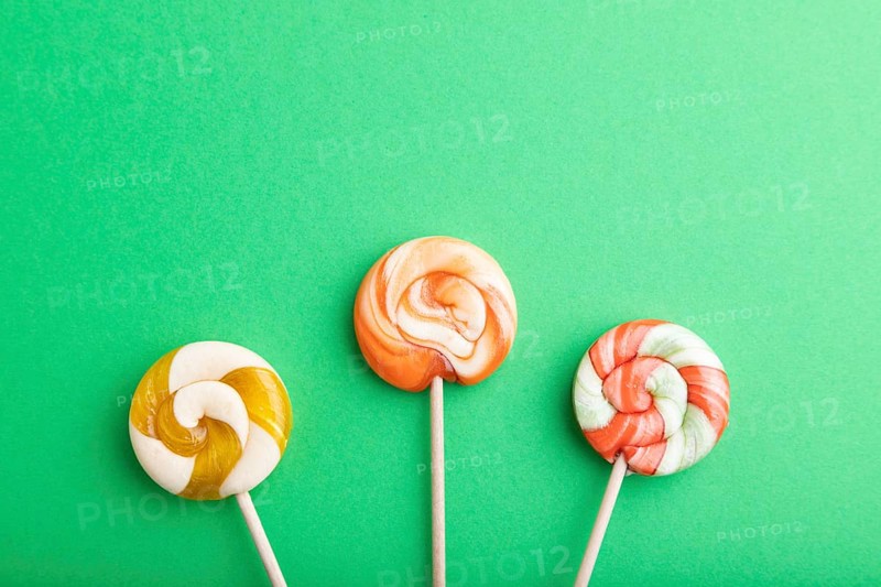 Three lollipop candies on green pastel background. copy space, top view, flat lay