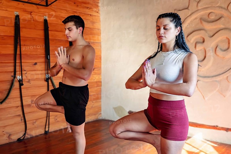 Young sporty couple practicing yoga class, man and woman with eyes closed in Vrksasana, tree pose, practicing balance, full body plane, in yoga studio. Wellness, wellness concept