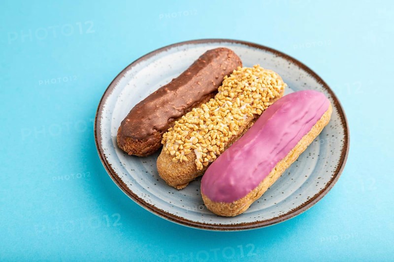 Set of eclair, traditional french dessert on ceramic plate on blue pastel background. side view, close up, still life. Breakfast, morning, concept