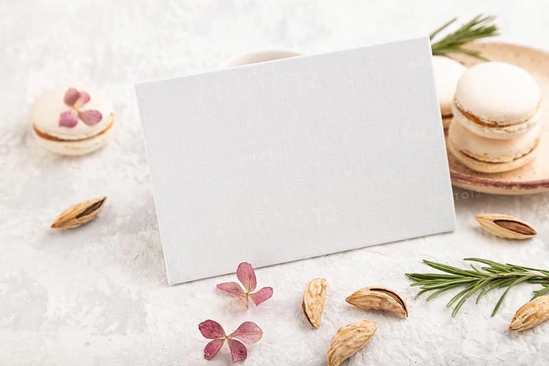 White business card mockup with cup of coffee, almonds and macaroons on gray concrete background. Blank, side view, still life