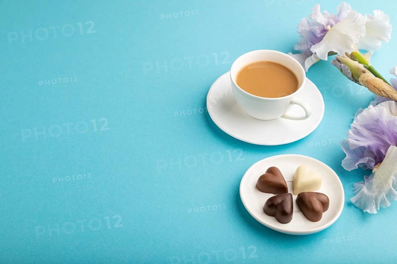 Cup of cioffee with chocolate candies and lilac iris flowers on blue pastel background. side view, copy space, still life. Breakfast, morning, spring concept