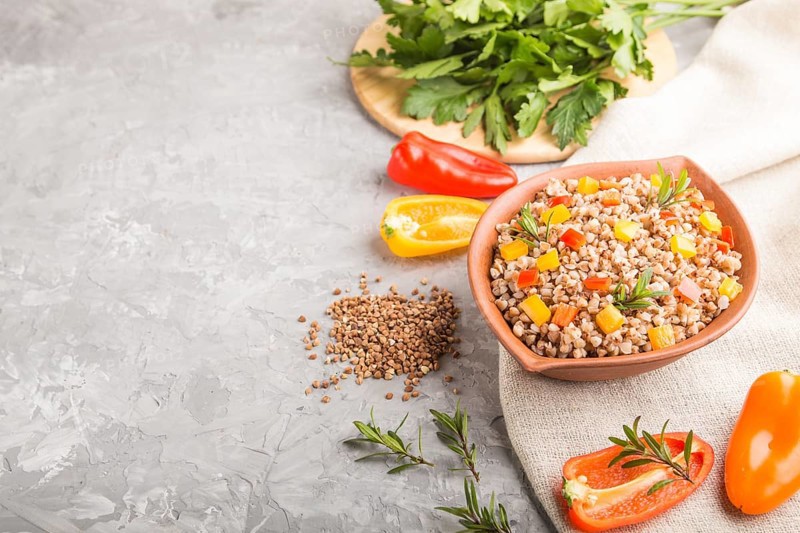 Buckwheat porridge with vegetables in clay bowl on a gray concrete background and linen textile. Side view, copy space. Russian traditional cuisine