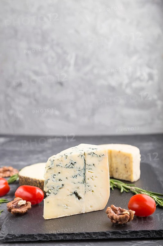 Blue cheese and various types of cheese with rosemary and tomatoes on black slate board on a black concrete background. Side view, copy space, selective focus