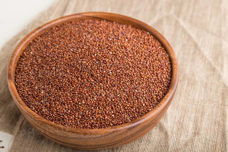 Wooden bowl with raw red quinoa seeds on a white wooden background and linen textile. Side view, close up, selective focus