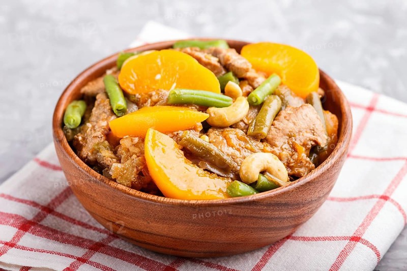 Fried pork with peaches, cashew and green beans in a wooden bowl on a gray concrete background. Side view, close up, chinese cuisine