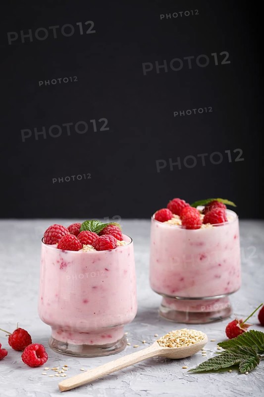 Yoghurt with raspberry and sesame in a glass and wooden spoon on gray and black background. side view, close up