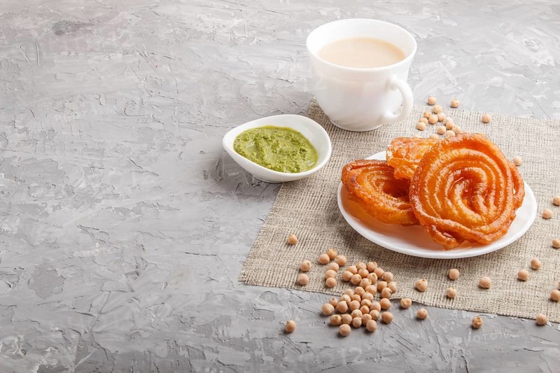 Traditional indian candy jalebi in white plate with mint chutney on a gray concrete background. side view, copy space