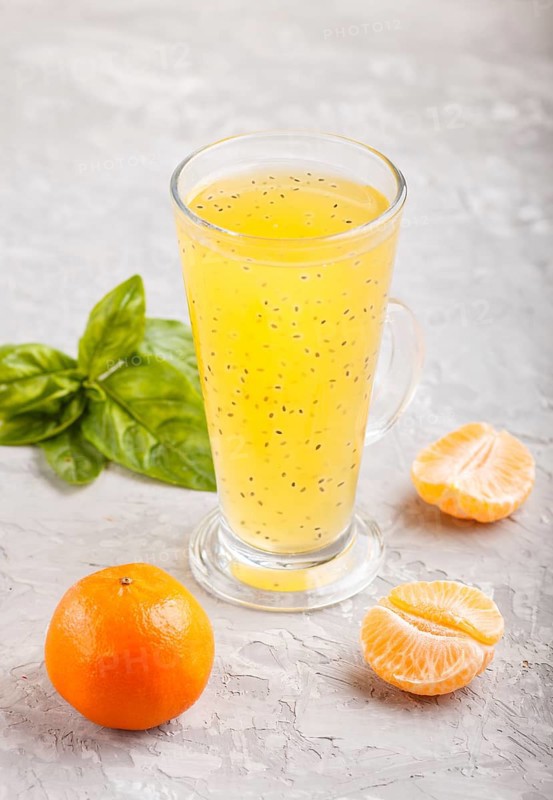 Glass of tangerine orange colored drink with basil seeds on a gray concrete background. Morninig, spring, healthy drink concept. Side view, copy space