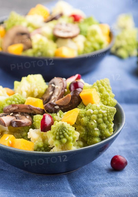 Vegetarian salad from romanesco cabbage, champignons, cranberry, avocado and pumpkin on a black concrete background and blue textile. side view, close up, selective focus