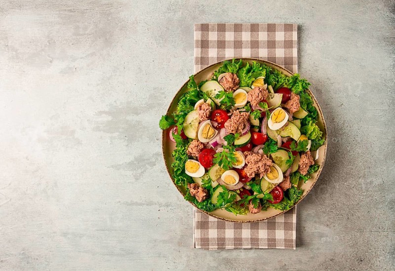 Tuna salad, vegetable salad with quail eggs, lettuce, red onion and cucumbers, on a light gray table, keto food, lifestyle, healthy eating, selective focus, top view, no people