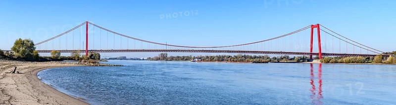 Panorama view from the left bank of the Rhine, western bank of the Rhine, of an earth-anchored suspension bridge with two abutments and red steel piers nicknamed the Golden Gate of the Lower Rhine over the River Rhine, with a total length of 1228 metres the longest suspension bridge in Germany, Emmerich, North Rhine-Westphalia, Germany, Europe