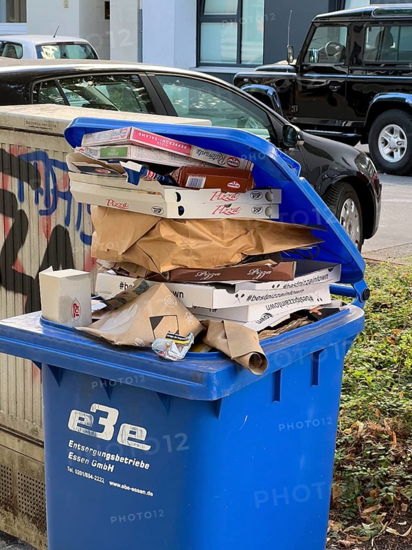 Overflowing waste paper bin, standing on a pavement, waiting to be emptied by a municipal waste disposal company, recycling