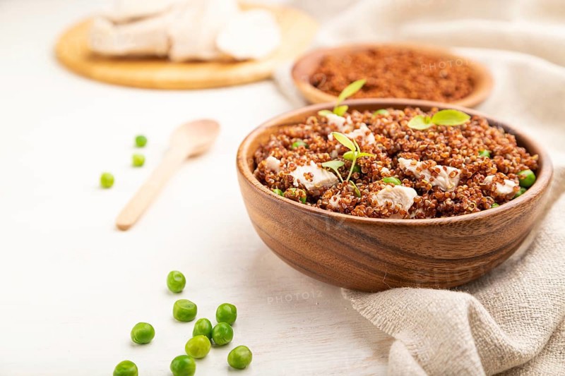 Quinoa porridge with green pea and chicken in wooden bowl on a white wooden background and linen textile. Side view, close up, selective focus