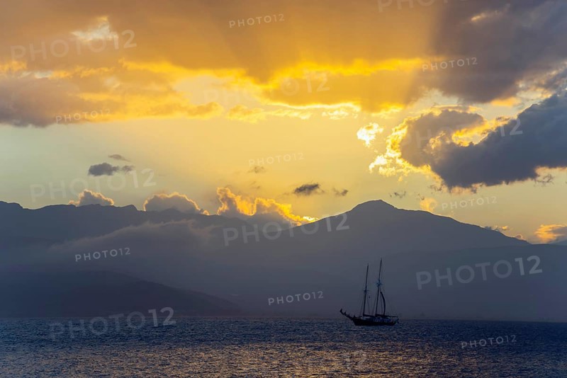A sailboat on the sea in front of a dramatic sunset, yellow rays of light over the mountains, Agia Kyriaki, Nafplio, Nauplia, Nauplion, Nafplion, Argolis, Argolic Gulf, Peloponnese, Greece, Europe