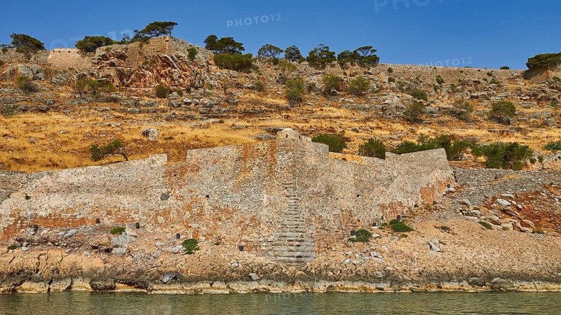 Old stone wall on rocky cliff with dry vegetation and calm sea water in the foreground, Venetian Sea Fortress, Leprosy Island, Spinalonga, Elounda Bay, Mirabello Bay, East Crete, Crete, Greek Islands, Greece, Europe